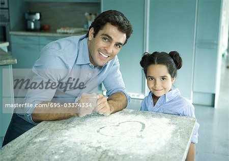 Père et fille debout de comptoir avec de la farine saupoudré sur elle, coeur dessiné dans la farine