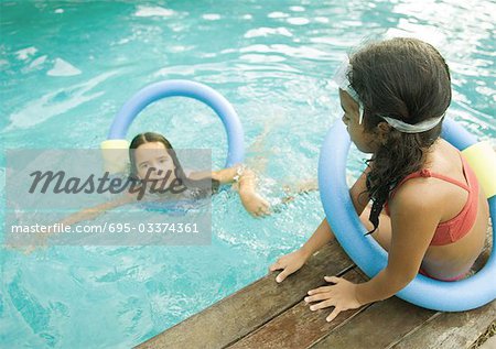 Zwei Mädchen mit schwebenden Ringe, einer im Pool, einer sitzt am Rand des Pools