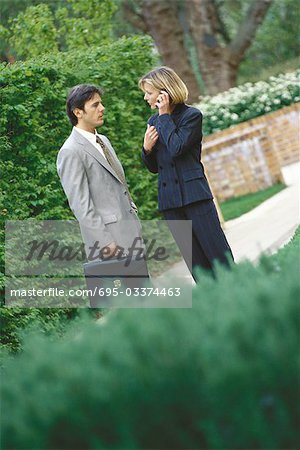 Male and female business associates standing outoors, woman using phone