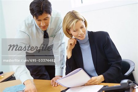 Business colleagues, man leaning over woman's shoulder, pointing to documents