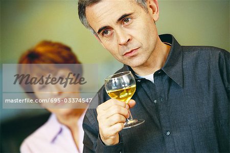 Senior man holding glass of wine, senior woman looking at him in background