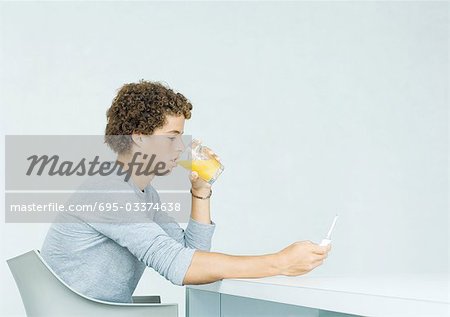 Teenage boy using cell phone, drinking juice