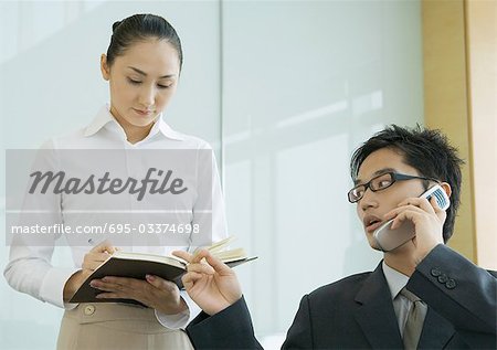 Businessman and female assistant, man using phone and gesturing to agenda