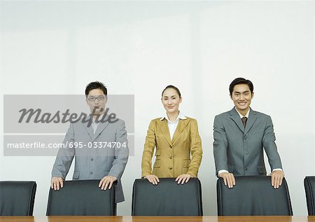 Business executives standing with hands on backs of chairs in conference room