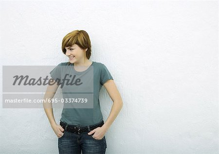 Young woman standing with hands in pockets, looking away, white background