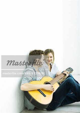 Junges Paar sitzt am Boden, Man Gitarre spielen