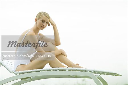 Teenage girl sitting on lounge chair, knee up, looking at camera