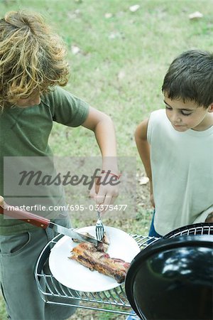 Deux garçons, debout à côté du barbecue, un découpage de la viande sur la plaque
