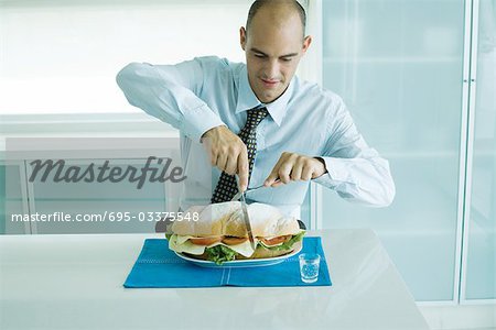 Mann schneiden in großen Sandwich mit Messer und Gabel