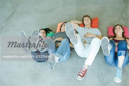 Vier Teen Freunde liegen am Boden, den Rücken halten Beine, konzentrieren sich auf die Sohlen der Schuhe