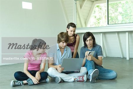 Quatre amis adolescents assis sur le plancher, à l'aide d'ordinateur portable