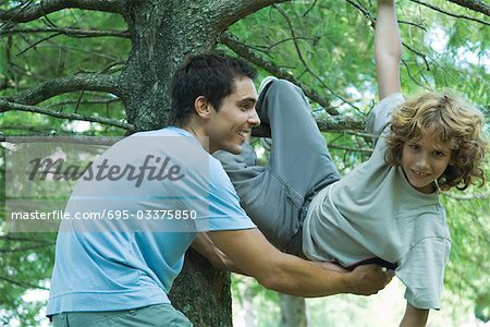 Boy climbing tree, father catching him