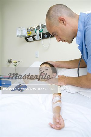 Boy lying in hospital bed, doctor taking pulse