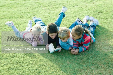 Children lying on grass together, reading