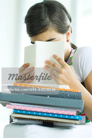 Teen girl avec pile de travail à domicile, se cachant le visage derrière le livre, portrait