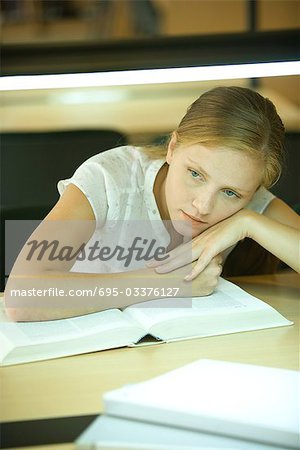 Young woman studying in university library, leaning on book and looking away