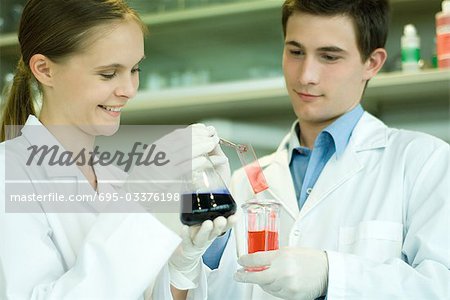 Young male and female scientists holding solutions in lab glassware