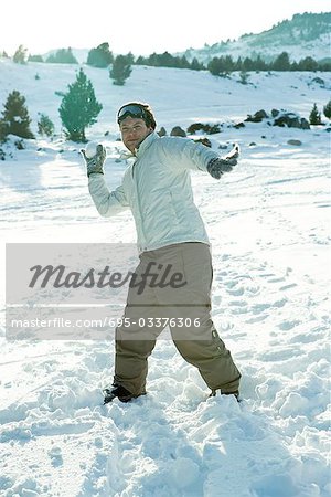 Young man throwing snowball, smiling at camera, full length