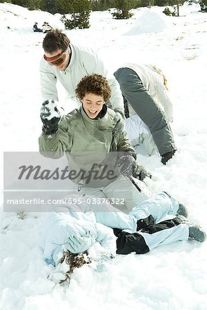 Young friends having snowball fight, one lying on ground, covering head with arms