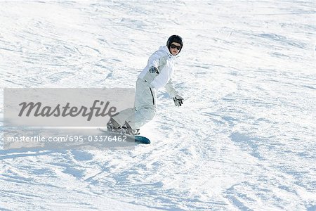 Adolescente, planche à neige vers le bas de la pente de ski, pleine longueur