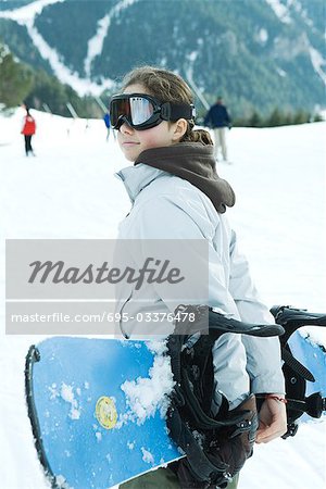Teenage girl carrying snowboard behind back, waist up