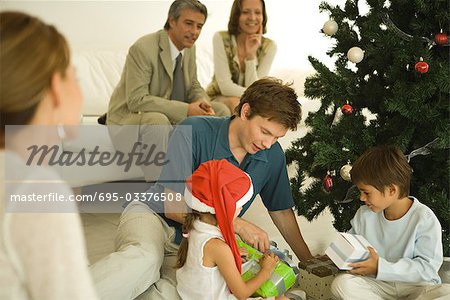 Vater und zwei Kinder sitzen am Weihnachtsbaum, Geschenke zusammen, Familie gerade öffnen