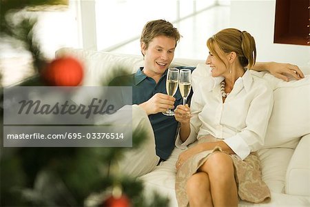 Couple faire un toast au champagne, souriant à l'autre, arbre de Noël au premier plan