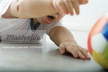 Baby lying on floor, reaching for ball, cropped view