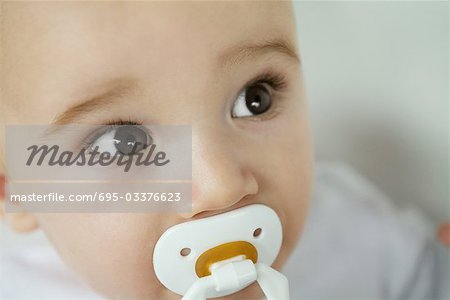 Baby with pacifier in mouth, raising eyebrows, close-up