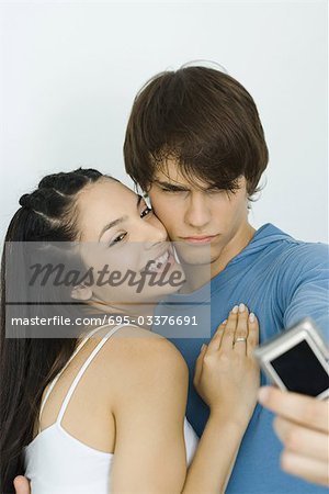 Jeune couple prenant autoportrait avec appareil photo numérique, femme, sourire aux lèvres, sourcils furrowing l'homme