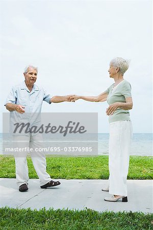 Senior couple dancing on sidewalk overlooking ocean, full length