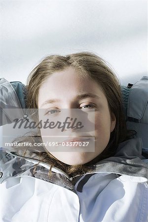 Teenage girl lying on snow with hands behind head, looking at camera