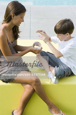 Teenage girl and younger brother sitting, looking at crystal ball together
