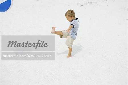 Junge treten Beach Ball am Strand, Seitenansicht