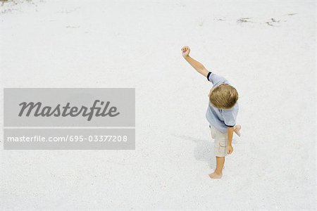 Young boy walking on the beach with one arm raised, high angle view