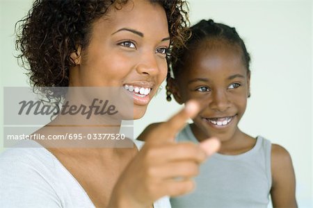 Young woman pointing finger and looking away with daughter, both smiling