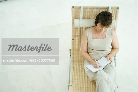 Femme assise sur la chaise de salon d'écriture dans le journal, vue grand angle