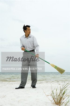 Man standing on beach sweeping with broom, looking away