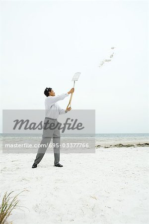 Man at the beach holding up shovel, throwing sand, full length