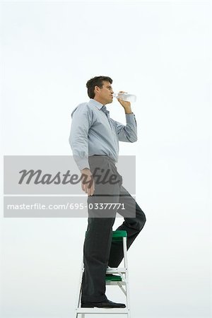 Man standing on top of ladder, drinking bottled water, side view