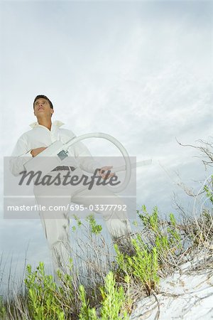Homme debout sur la dune de sable, tenant l'aspirateur, en levant