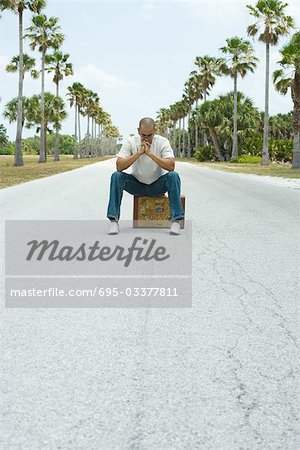 Man sitting on suitcase in the middle of street, head down