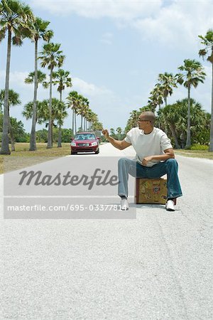 Homme assis sur la valise au milieu de la rue, regarder par-dessus l'épaule à l'approche de voiture