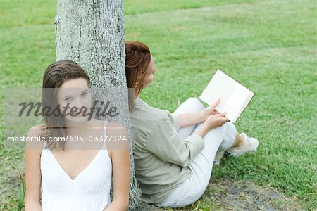 Mère et fille, appuyé contre le tronc d'arbre, livre de lecture de femme, adolescente, souriant à la caméra