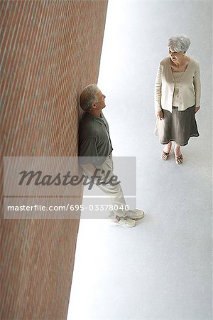 Couple talking together, man leaning against wall with hands in pockets, high angle view