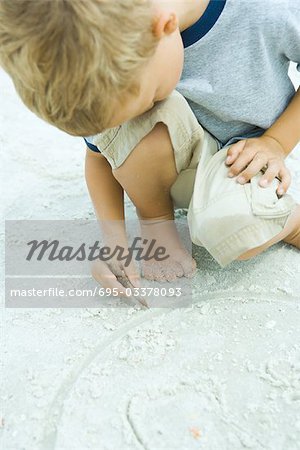 Petit garçon accroupi sur la plage, dans le sable avec le bâton, la tête sur les genoux de dessin