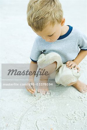 Kleiner Junge am Strand, hockend Zeichnung in Sand mit stick
