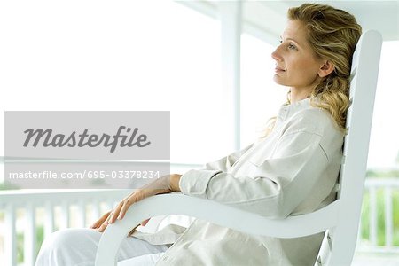 Femme assise dans le fauteuil à bascule sur la véranda, vue latérale
