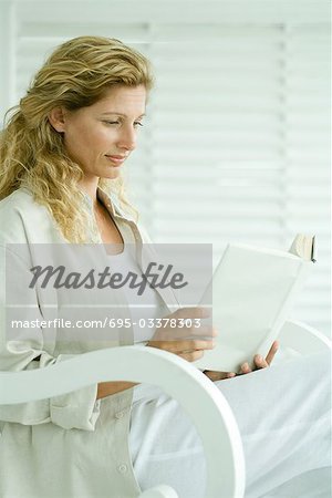 Woman sitting in rocking chair, reading book, smiling