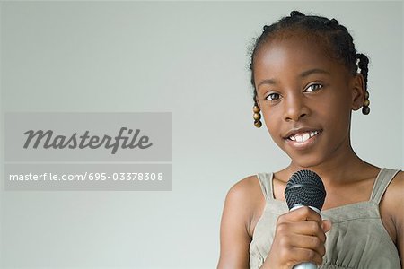 Petite fille tenant micro, souriant à la caméra, portrait